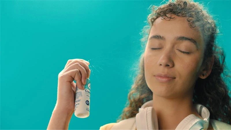 Mujer joven con cabello rizado aplica el spray CUIDADERM de JGB en su rostro