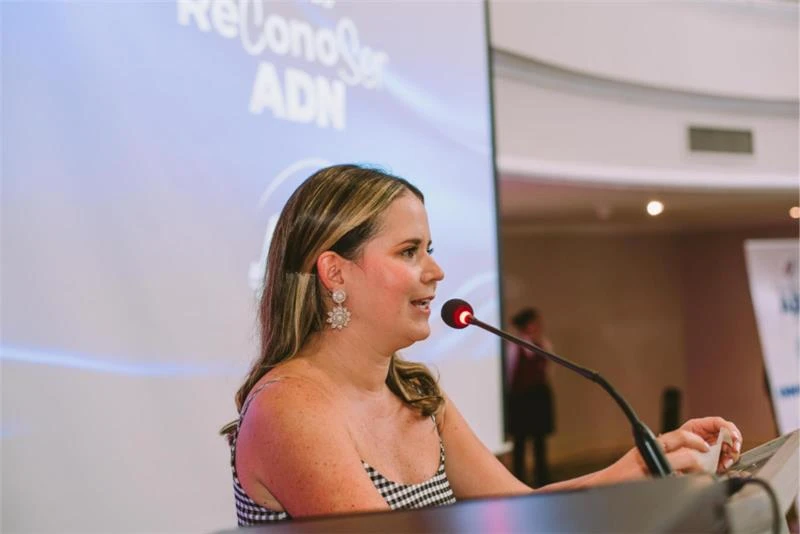 Una mujer sonríe mientras ofrece un discurso en los Premios ReconoSer desde el podio con micrófono y con una pantalla de fondo