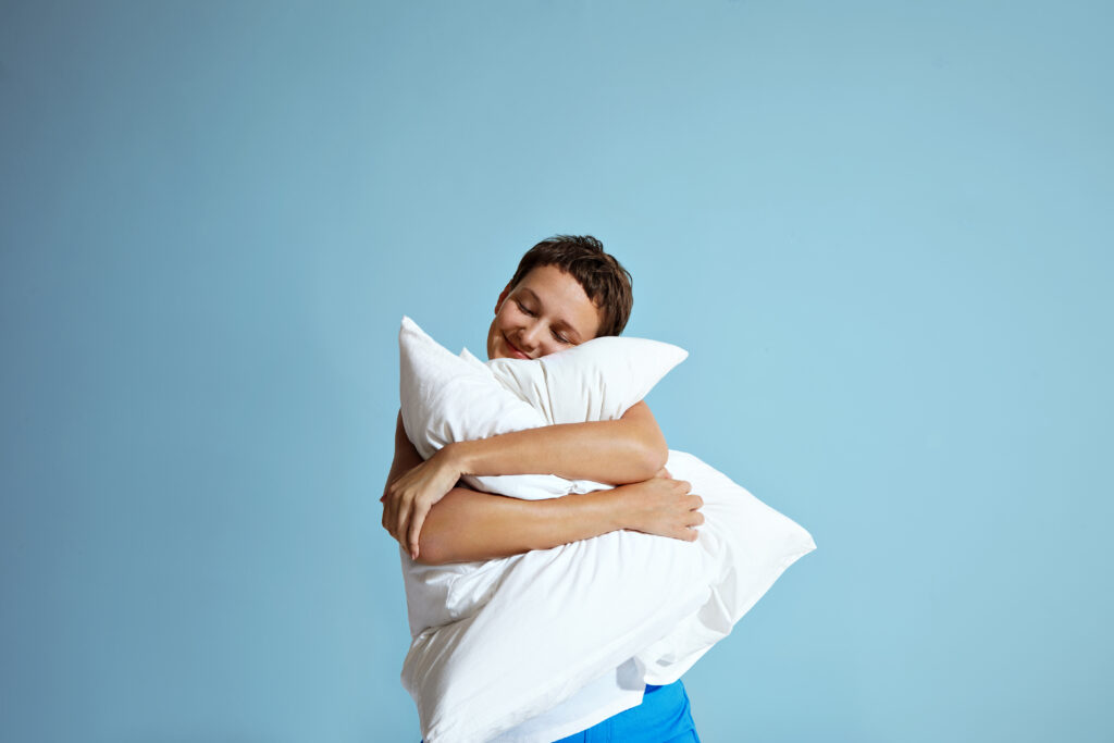 Persona abrazando una almohada con expresión de satisfacción asociada a un descanso de calidad.