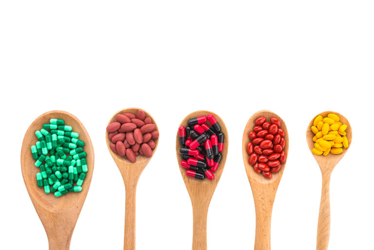 Diferentes tipos de vitaminas en tableta en unas cucharas.