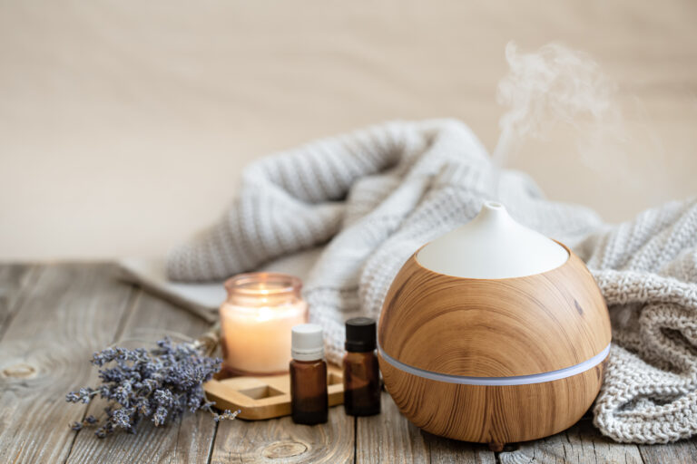 Difusor de madera evaporando esencia junto a un ramo de lavanda seca, frascos de aceite y una vela encendida.