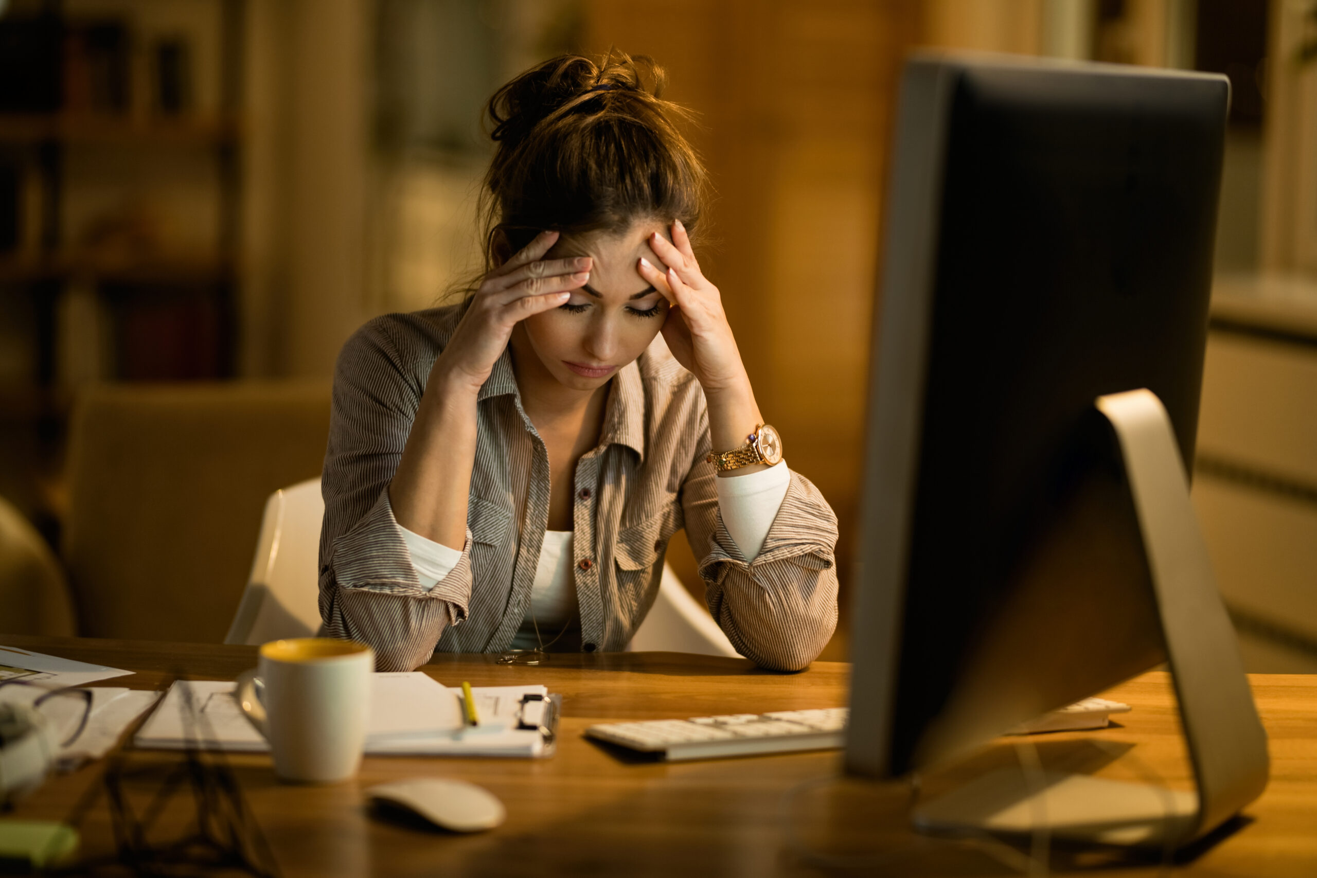 Mujer trabajando frente al computador con signos de tensión y cansancio relacionados con el estrés laboral