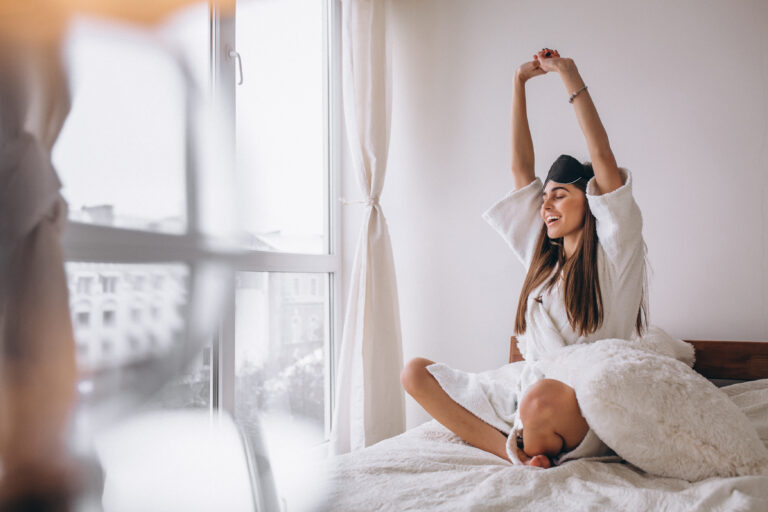Mujer estirándose al despertar en la cama después de una noche de sueño reparador.