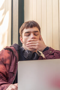 Hombre jóven bostezando mientras mira su portatil debido a la falta de energía.