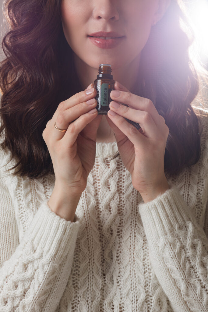 Mujer sosteniendo un frasco pequeño de aceite esencial cerca de su rostro para disfrutar de su aroma.