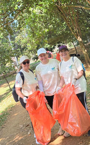 Tres colaboradoras de JGB sostienen bolsas con residuos recolectados durante una jornada de limpieza ambiental en un parque.