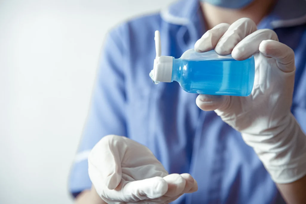 Frasco de agua oxigenada en las manos de un médico que lo está vertiendo en sus manos.